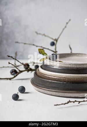 Baies de Blackthorn avec feuilles vertes et jaunes dans des assiettes faites à la main en céramique sur fond clair. Copier l'espace. Banque D'Images