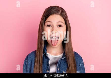 Photo portrait du port de jeans veste petite fille grimacing montrant la langue isolée sur fond rose pastel Banque D'Images