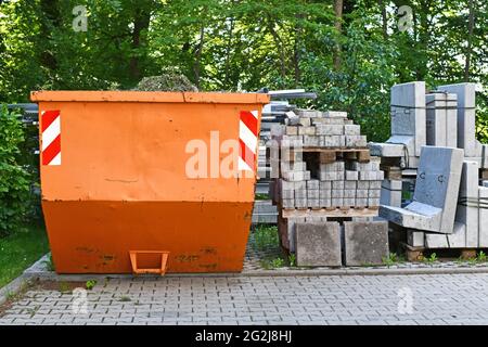Conteneur à benne à ordures transportable industriel orange et pierres en forme de galets sur palette sur le chantier de construction Banque D'Images