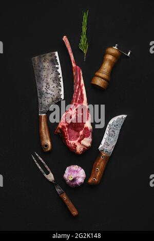 Composition en hauteur avec steak de cowboy de bœuf cru et outils de boucher sur fond arrière-plan Banque D'Images