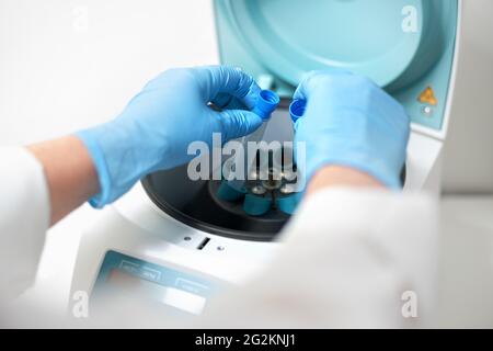 Main de la femme dans un gant bleu mettant des échantillons d'analyse dans une centrifugeuse en laboratoire. Une chercheuse place des tubes à essai dans la machine spéciale. Banque D'Images