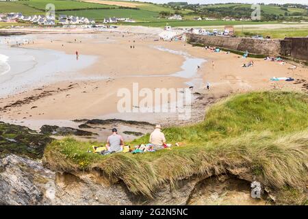 Garrettstown, Cork, Irlande. 12 juin 2021. Un jeune couple s'assoit et lit sur les pistes d'herbe donnant sur la plage de Garrettstown, Co. Cork, Irlande. - crédit; David Creedon / Alamy Live News Banque D'Images