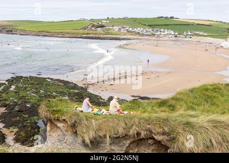 Garrettstown, Cork, Irlande. 12 juin 2021. Un jeune couple s'assoit et lit sur les pistes d'herbe donnant sur la plage de Garrettstown, Co. Cork, Irlande. - crédit; David Creedon / Alamy Live News Banque D'Images