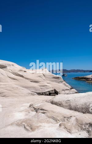 Île de Milos, Sarakiniko. Cyclades Grèce. Paysage lunaire, formations rocheuses de couleur blanche, falaises et grottes, mer bleue ondulée et fond ciel clair. Banque D'Images