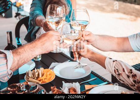 Rognez la photo des mains de la fête des amis sur le patio au-dessus d'un verre de vin blanc. Concept de vacances communes Banque D'Images