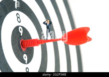 Hommes d'affaires debout au-dessus de la flèche rouge sur le plan de travail à l'aide de jumelles. Photo miniature de jouets de personnes minuscules. Isolé sur fond blanc. Banque D'Images