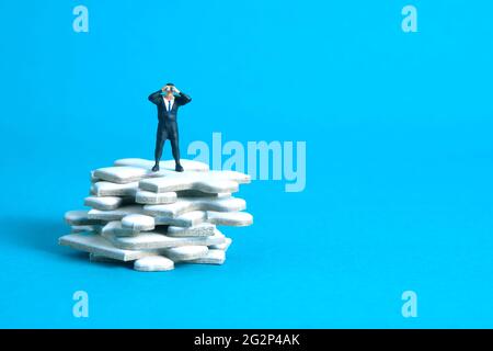 Les hommes d'affaires se tenant au-dessus de la pile de pièces de puzzle utilisant des jumelles au-dessus de la table en bois. Photo miniature de jouets de personnes minuscules. Isolé sur bac bleu Banque D'Images