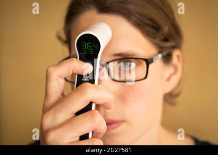 Une jeune femme de la trentaine a diagnostiqué une fièvre en prenant sa propre température à l'aide d'un thermomètre infrarouge numérique. ROYAUME-UNI Banque D'Images
