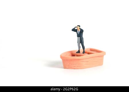 Homme d'affaires utilisant des jumelles debout au-dessus du bateau. Photo miniature de jouets de personnes minuscules. Isolé sur fond blanc Banque D'Images