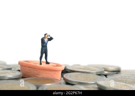 Homme d'affaires utilisant des jumelles se tenant au-dessus du bateau et pile de monnaie. Photo miniature de jouets de personnes minuscules. Isolé sur fond blanc Banque D'Images