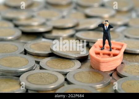 Homme d'affaires utilisant des jumelles se tenant au-dessus du bateau et pile de monnaie. Photo miniature de jouets de personnes minuscules. Isolé sur fond blanc Banque D'Images