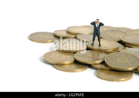 Homme d'affaires utilisant des jumelles se tenant au-dessus de la pile de monnaie. Photo miniature de jouets de personnes minuscules. Isolé sur fond blanc Banque D'Images