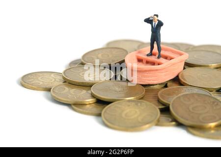 Homme d'affaires utilisant des jumelles se tenant au-dessus du bateau et pile de monnaie. Photo miniature de jouets de personnes minuscules. Isolé sur fond blanc Banque D'Images