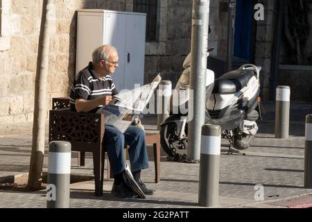 Jérusalem, Israël - 3 juin 2021 : un homme âgé lisant le quotidien sur un banc dans une rue de Jérusalem, Israël, par beau temps. Banque D'Images