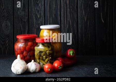 Tomates rouges et jaunes fermentées et concombres avec légumes sur fond sombre. Plats végétariens. Tomates salées et concombres. Bio mariné Banque D'Images