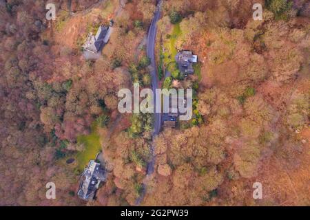 Tir de drone aérien de la route asphaltée menant à travers les bois. Lake District, Royaume-Uni. Banque D'Images