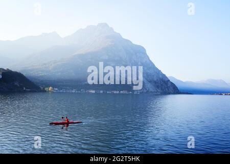 Lecco, Italie - 8 novembre 2020 : kayak, canoë, pagayage sur le lac de montagne de Côme au lever ou au coucher du soleil. Homme kayakiste en kayak rouge. Actif Banque D'Images