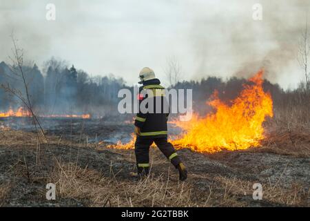 Un pompier éteint l'herbe sèche. Un pompier lutte contre un incendie dans une zone ouverte. Mesures de secours contre les flammes. Une catastrophe écologique brûlée Banque D'Images