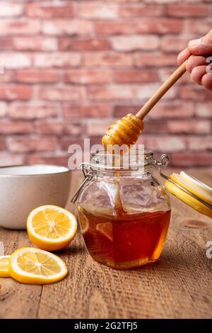 Pot de miel égoutté d'un bâton de miel avec un côté de citron sur une table en bois Banque D'Images