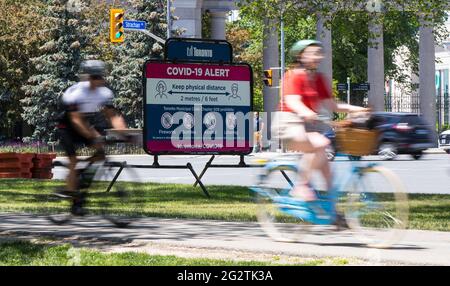 Toronto, Canada. 12 juin 2021. Les cyclistes passent devant un panneau d'affichage rappelant aux gens de pratiquer la distanciation physique à Toronto, Canada, le 12 juin 2021. Le Canada a signalé 1,115 nouveaux cas quotidiens de COVID-19 samedi, portant le total cumulatif à 1,400,827, dont 25,910 décès, selon CTV. Credit: Zou Zheng/Xinhua/Alamy Live News Banque D'Images