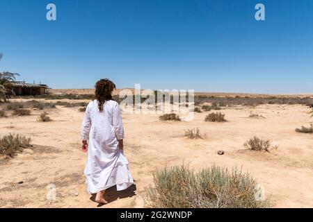 Une femme se tient dans le désert et regarde l'horizon. Vêtements blancs qui flottent dans le vent. Concept de détente, de recherche intérieure, de méditation, de tranquillité d'esprit. Photo de haute qualité Banque D'Images