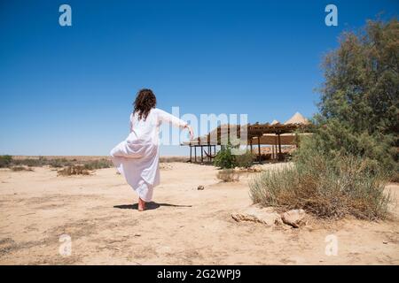 Une femme se tient dans le désert et regarde l'horizon. Vêtements blancs qui flottent dans le vent. Concept de détente, de recherche intérieure, de méditation, de tranquillité d'esprit. Photo de haute qualité Banque D'Images