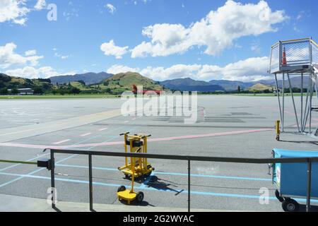 Queenstown, Nouvelle-Zélande - mars 6 2015 ; les montagnes forment le décor d'un avion de couleur orange arrivant à l'aéroport à distance en traversant le tarmac. Banque D'Images