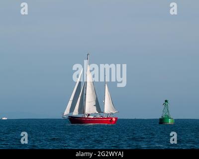 Yacht de style classique avec coque rouge navigue après une bouée verte sur une belle mer bleu profond. Banque D'Images