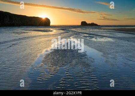 Le sable se déforme et une rivière mène l'œil du spectateur vers Chapel Rock sur la plage Perranporth de Cornwall. L'image a été capturée peu avant le coucher du soleil Banque D'Images