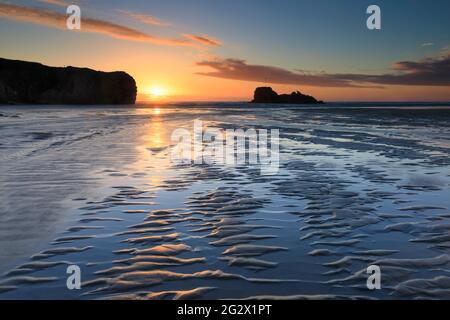 Le sable se déforme et une rivière mène l'œil du spectateur vers Chapel Rock sur la plage Perranporth de Cornwall. L'image a été capturée peu avant le coucher du soleil Banque D'Images