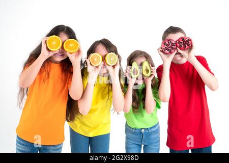 Trois filles et un garçon utilisant des fruits comme lunettes sur un fond blanc. Groupe d'enfants heureux avec des mains d'orange, de citron, d'avocat et de grenade Banque D'Images