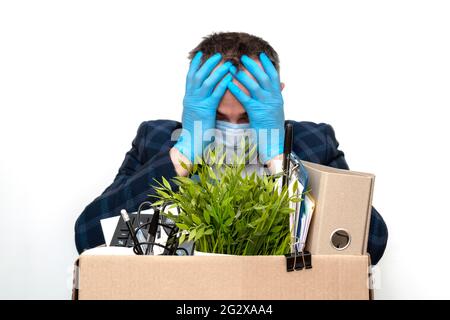 Congédiement homme dans des gants de protection médicale bleus et un masque médical tient sa tête dans ses mains. Dépression et désespoir. L'accent sur la boîte de boîte avec Banque D'Images
