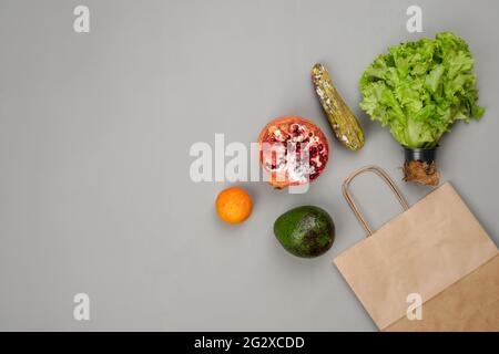 Légumes et fruits pourris avocat, mandarine, laitue, paquet, grenade sur fond gris. Le concept de livraison de produits sous-standard. Banque D'Images