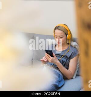 Jeune femme attentionnés assise à l'intérieur à la maison salon canapé utilisation des réseaux sociaux sur le téléphone pour discuter et rester en ligne elle est en contact avec son aimé Banque D'Images