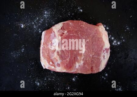 Morceau de porc cru avec du sel sur fond noir. Vue en hauteur d'un morceau de porc désossé frais. Gros morceau de viande. Concept de cuisine. Banque D'Images