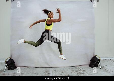 Jeune femme athlète en vêtements de sport avec la coupe du corps saut en plein air. African sportswoman faire de la course à pied et de la fente exercice mi-air pleine longueur Banque D'Images