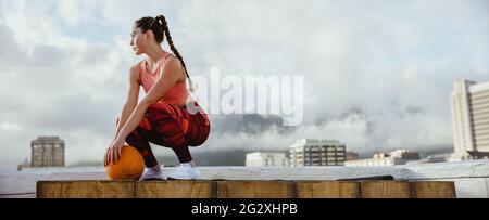 FIT femme portant des vêtements de sport avec le basket-ball prenant une pause de l'entraînement sur le toit. Athlète féminine assise sur le toit pour se détendre après l'exercice. Banque D'Images