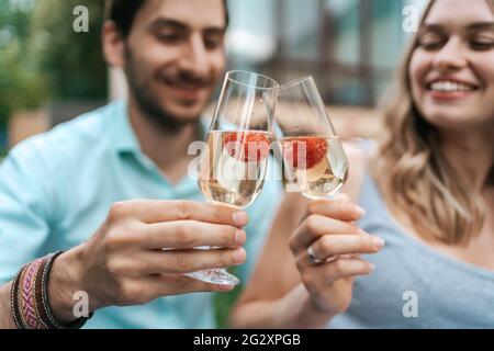 Portrait de couple heureux clinquant deux verres avec vin mousseux et fraises à l'intérieur avec maison floue sur fond. Célébrer l'amour Banque D'Images
