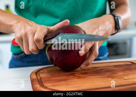 femme coupant une mangue dans la cuisine sur une planche de bois Banque D'Images