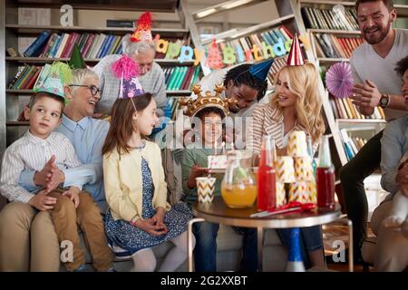 Famille et amis chantant et applaudissant lors de la célébration d'un anniversaire d'enfant dans une atmosphère festive à la maison. Famille, célébration, ensemble Banque D'Images