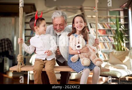 Grand-père jouant avec des petits-enfants sur l'oscillation dans une atmosphère joyeuse à la maison. Famille, loisirs, ensemble Banque D'Images