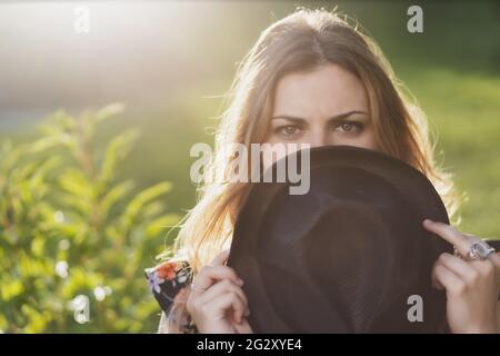 Gros plan portrait d'une belle fille cachant son visage derrière un chapeau en journée ensoleillée. Horizontalement. Banque D'Images