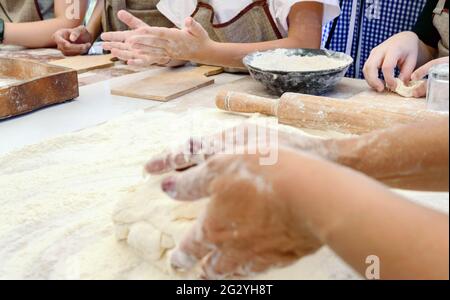 Le cuisinier enseigne aux enfants à faire de la pâte. La main femelle pétrit la pâte sur une table farinée. Classe de maître dans la cuisson. Cuisiner à la maison. Banque D'Images