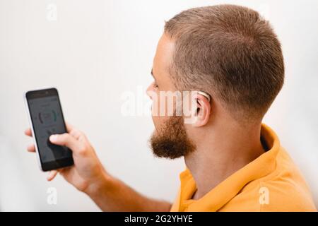 L'homme malentendant règle les paramètres de son aide auditive BTE via un smartphone. Prothèses auditives, traitement de la surdité, technologies innovantes en audiologie Banque D'Images