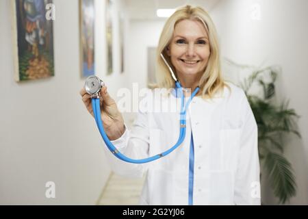 profession de médecin. Généraliste expérimentée portant un manteau médical avec stéthoscope à la main, debout dans une clinique médicale, portrait Banque D'Images