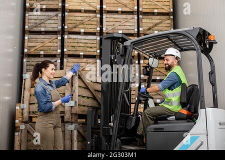 Employé sur chariot élévateur électrique porte le conteneur avec des pommes mûres à la caméra de stockage, le gestionnaire avec la tablette montre la direction Banque D'Images