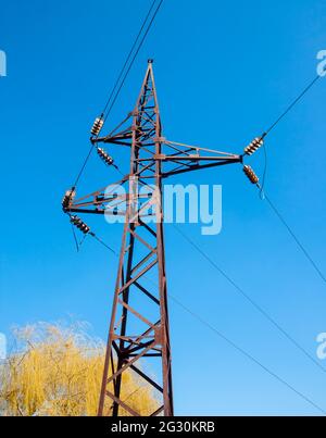 Vieux poteau haute tension rouillé contre le ciel bleu et saule jaune sur le fond Banque D'Images