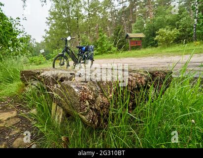 Banc abîmé depuis un tronc d'arbre dans un espace de repos de randonnée en face d'un vélo noir garé pendant une balade à vélo Banque D'Images