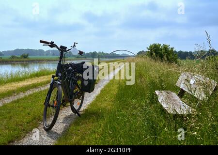 Vélo noir debout sur la voie de service à côté d'un canal en Allemagne, devant un banc pendant une pause en vélo Banque D'Images