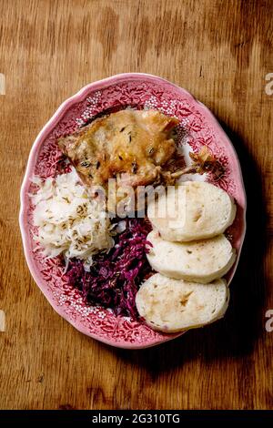 Pattes de canard cuites au four avec des pétrir de pain cuit en tranches et de la choucroute dans une assiette en céramique sur fond de bois brun. Tchèque traditionnel, allemand et européen Banque D'Images